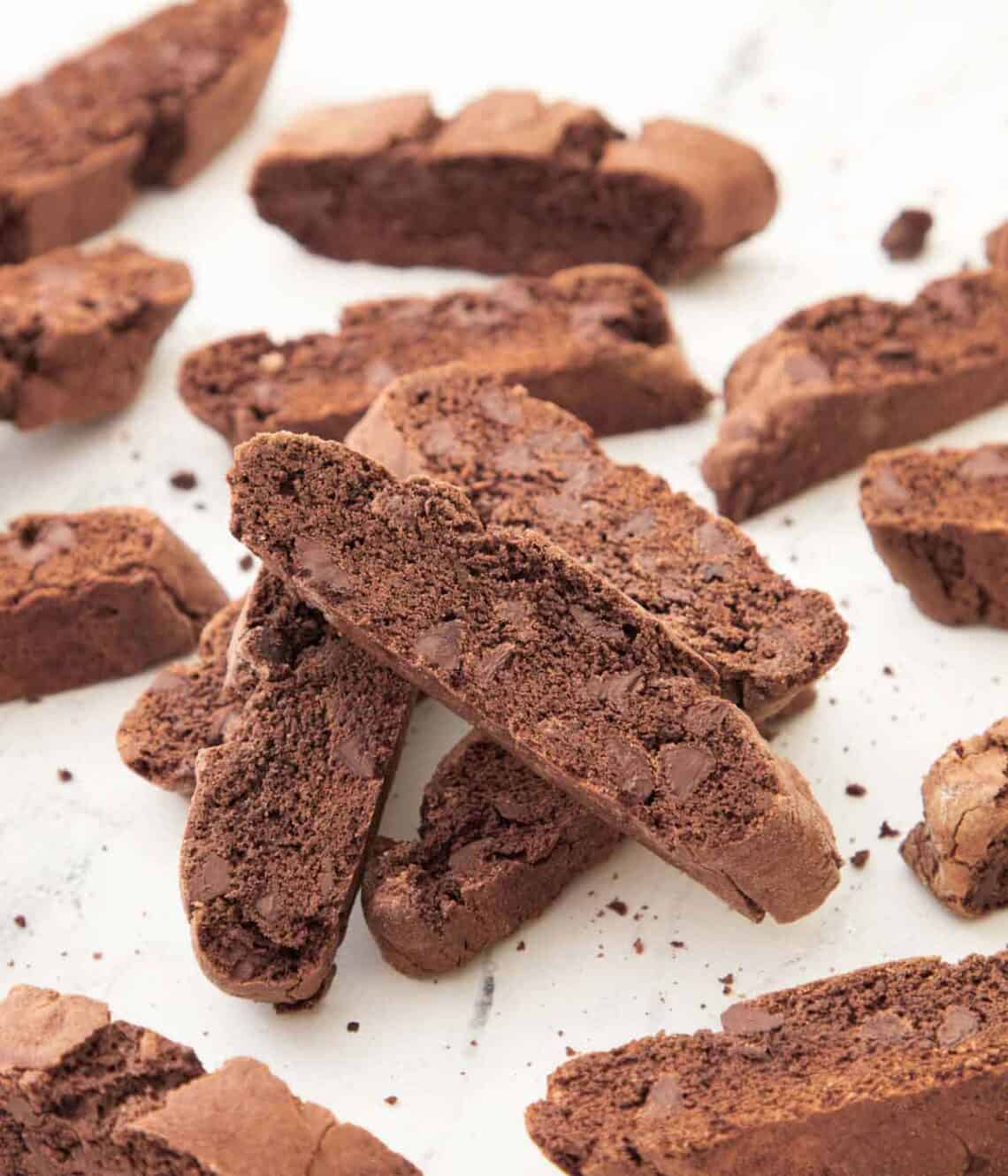 Multiple chocolate biscottis stacked on top of each other with more around it.