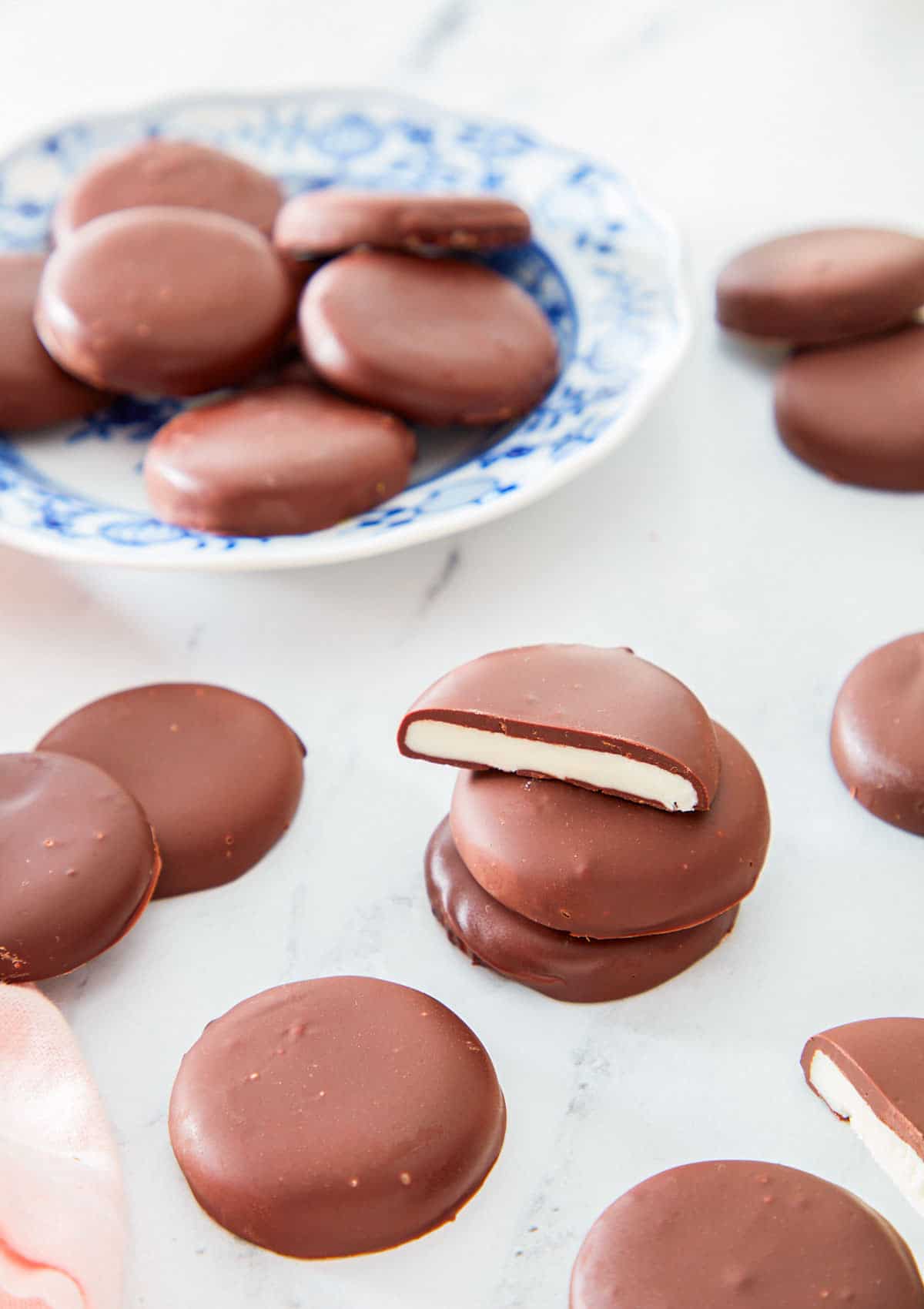 Multiple peppermint patties scattered with the focus on a stack of three in the middle, the top one cut in half.