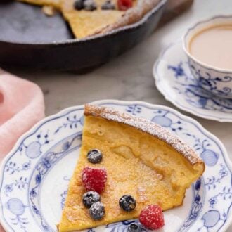 Pinterest graphic of a slice of Dutch baby with fresh berries and powdered sugar dusted on top.
