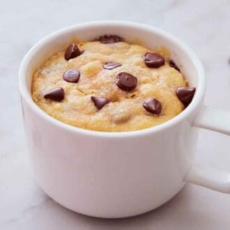 A white mug with a cookie baked inside with chocolate chips on top.