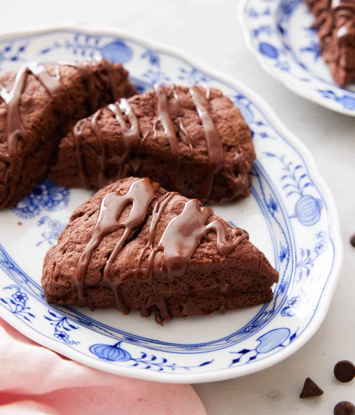 A platter with three chocolate scones with a linen and chocolate chips off to the side.