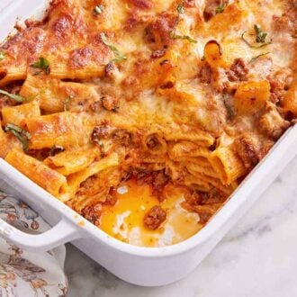 A slightly angled overhead view of a baking dish of baked rigatoni with a serving removed.