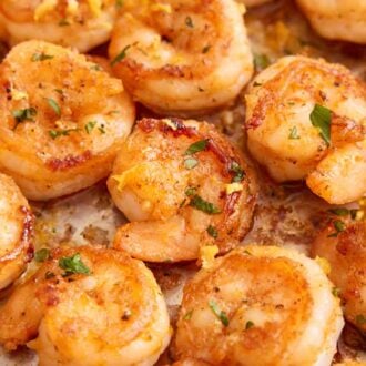 Close up view of sautéed shrimp in a single layer with lemon zest and parsley.