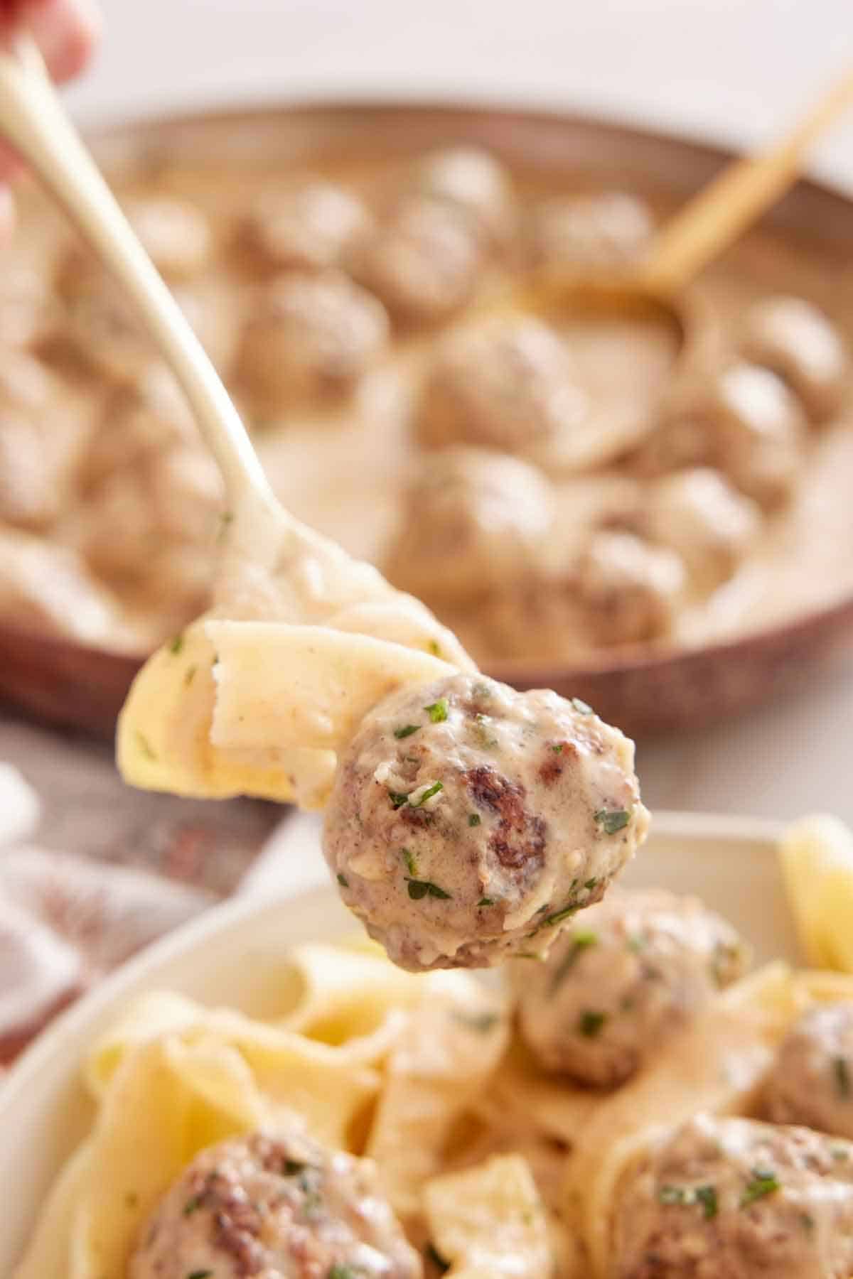 A fork lifting out a Swedish meatball and a noodle with sauce all over.