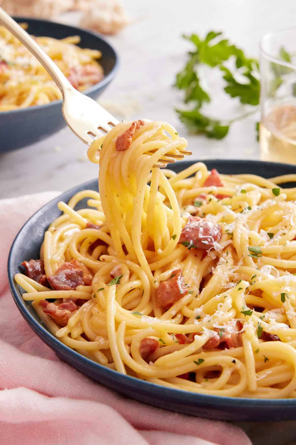 A fork lifting up spaghetti from a plate of pasta carbonara.
