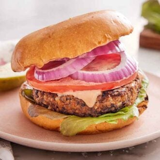 A plate with a veggie burger with a cut pickle in behind it.