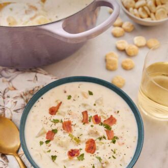 Pinterest graphic of a bowl of clam chowder with diced bacon on top with crackers and a purple pot in the background.
