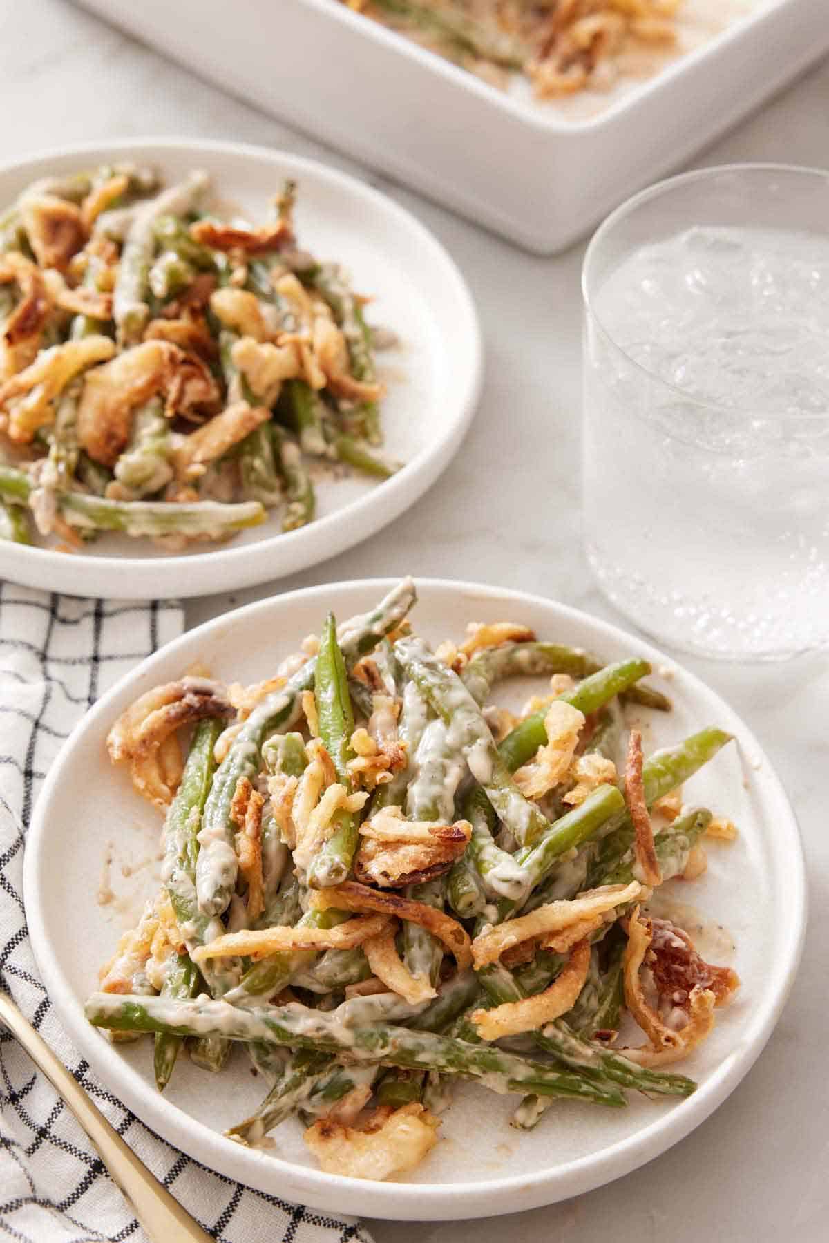 Two plates of green bean casserole with a glass of ice water.