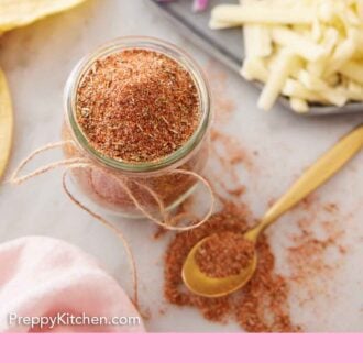 Pinterest graphic of an overhead view of a jar of taco seasoning with a spoonful places beside it. Some taco toppings on the side, out of focus.