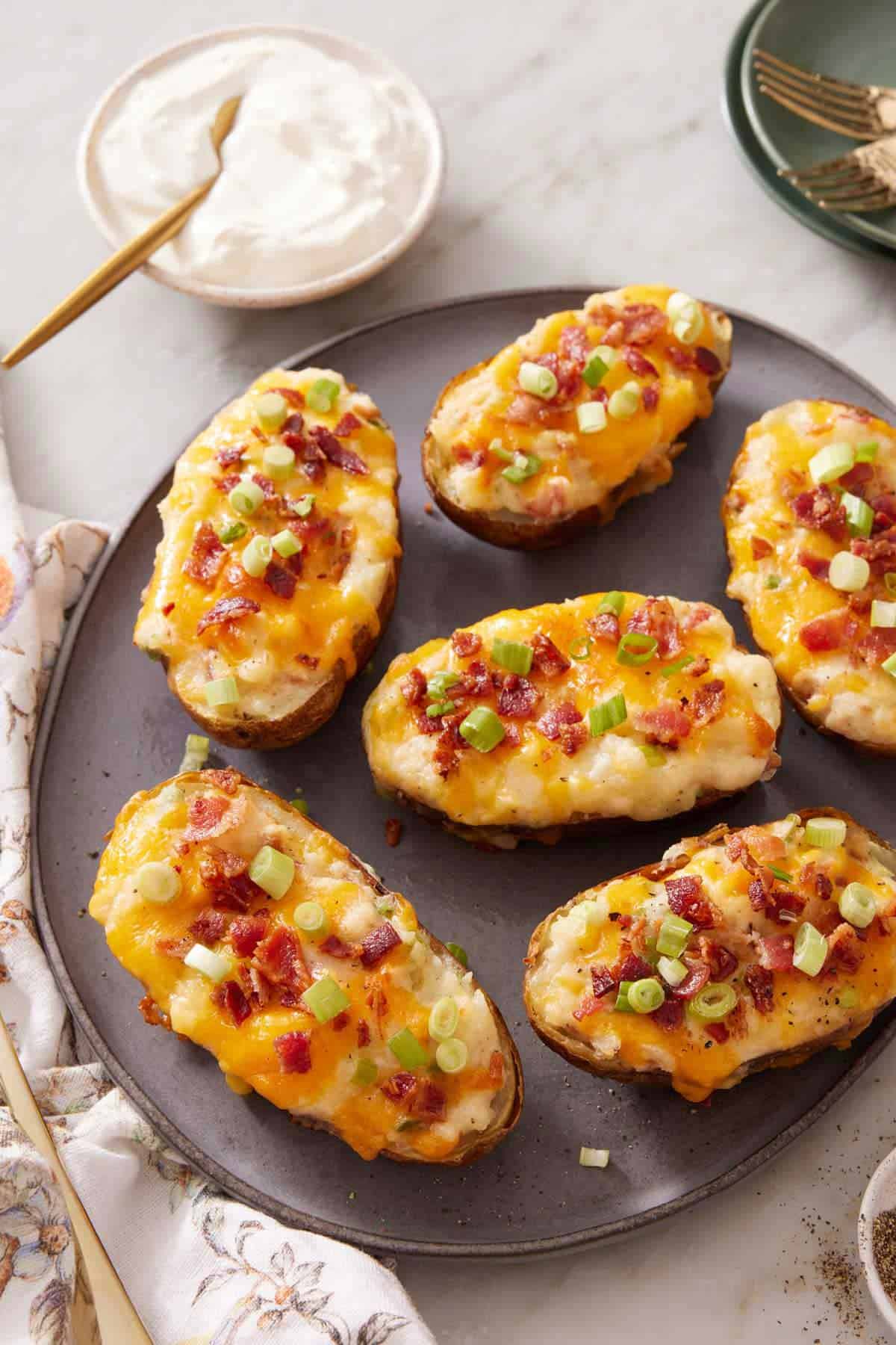 A platter with multiple twice-baked potatoes with a bowl of sour cream in the background.