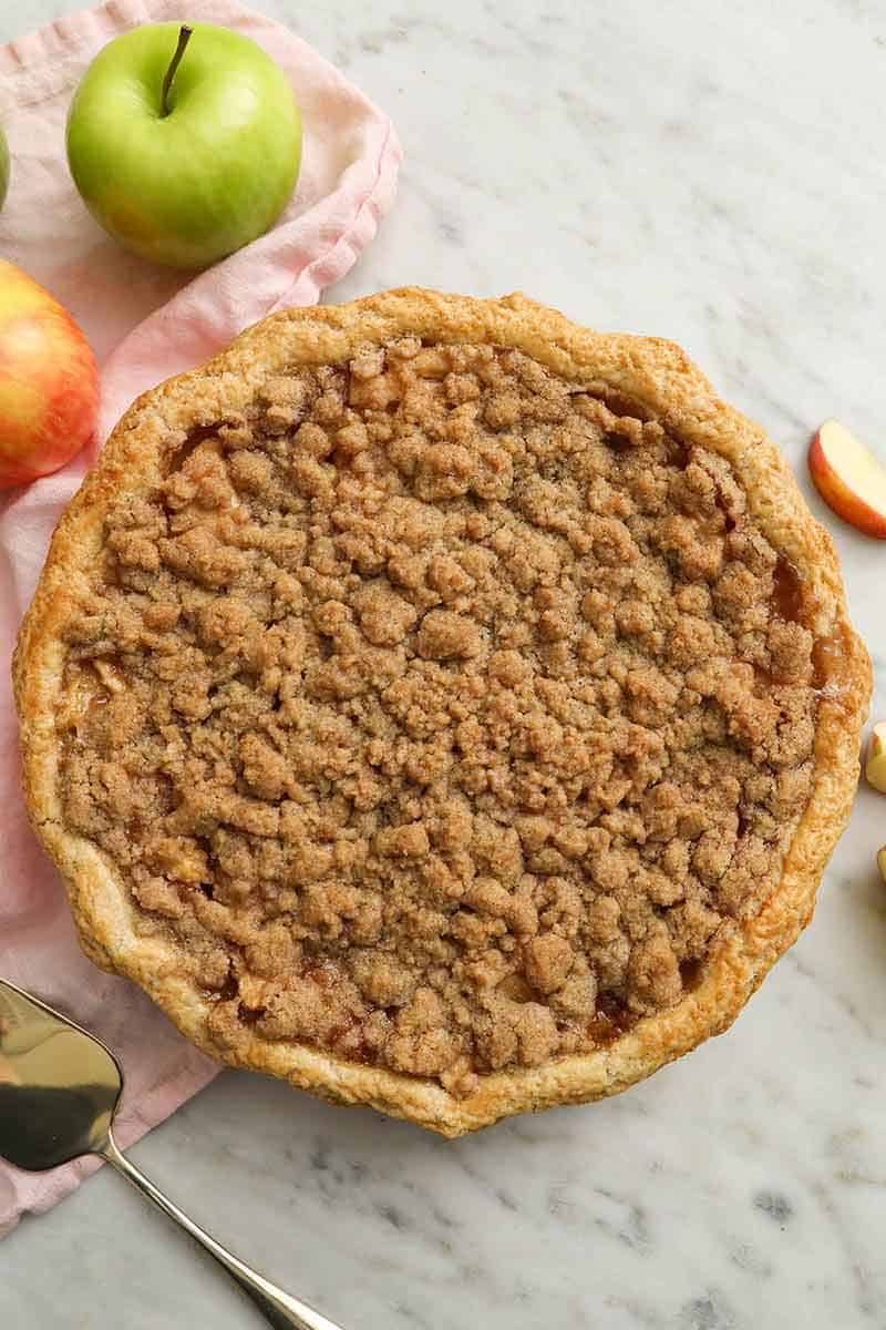 Overhead view of an entire apple crumble pie with some apples and apple slices around it.