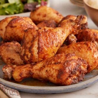 A platter of baked chicken legs with sides in the background.