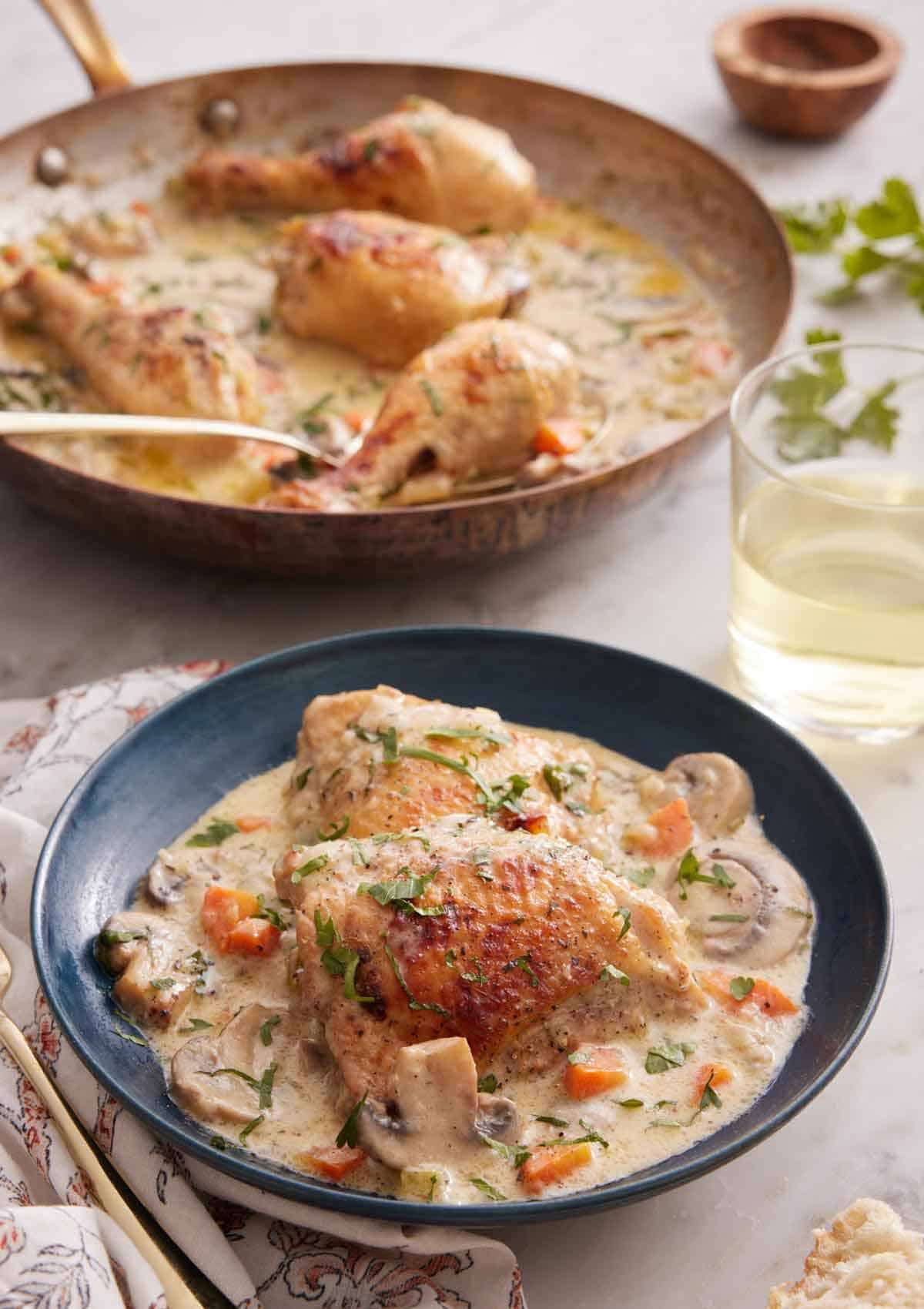 A plate with a serving of chicken fricassée with a skillet with more in the background.