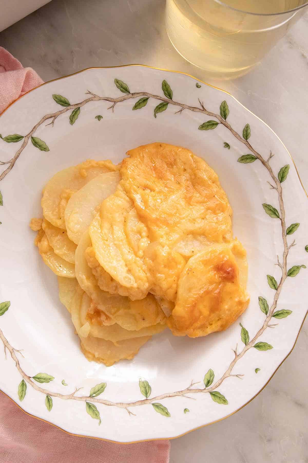 An overhead view of a plate of au gratin potatoes with a glass of wine beside it.