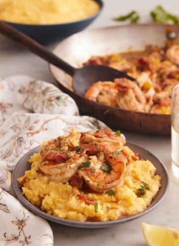 A bowl of shrimp and grits with a skillet of shrimp and bowl of grits in the background.