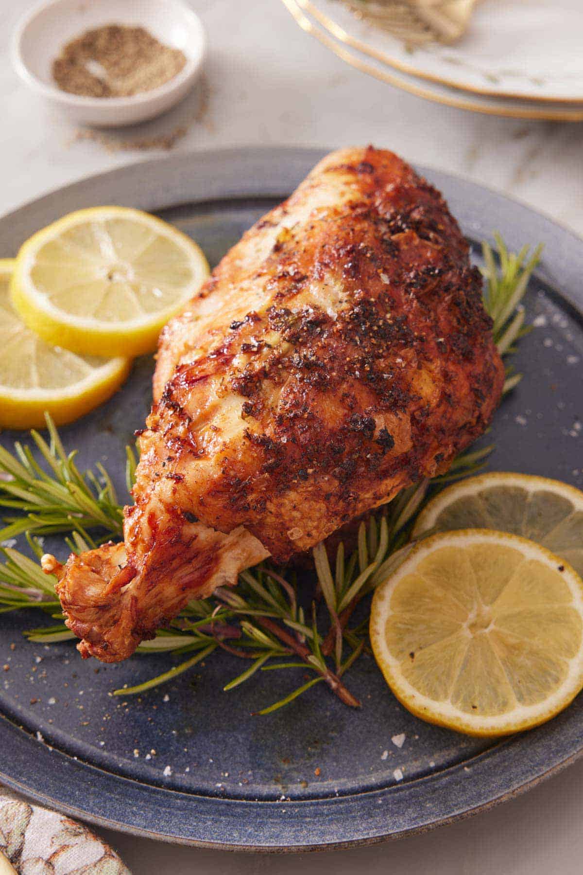 A plate with an air fryer turkey breast on top of fresh rosemary and slices of lemon.