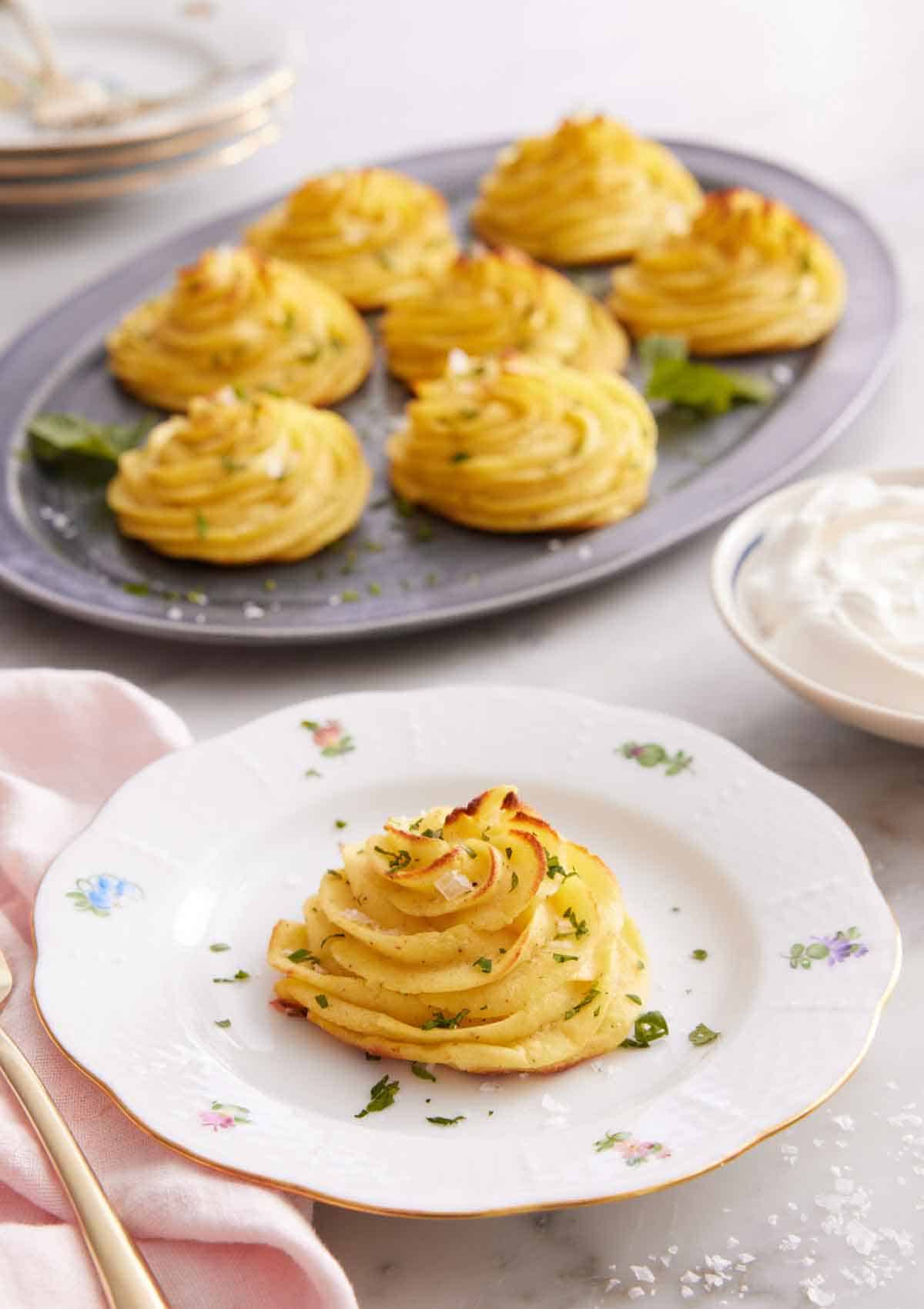 A plate with a serving of duchess potatoes with a platter with more in the background.