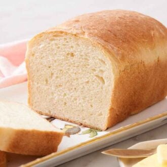 A loaf of potato bread on a platter with two slices cut.