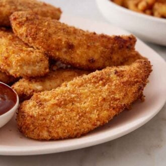 A platter of air fryer chicken tenders with a small bowl of bbq sauce.