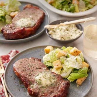 Pinterest graphic of a plate with an air fryer steak with a side of salad. An additional plated serving in the background along with a platter of salad and herb butter.