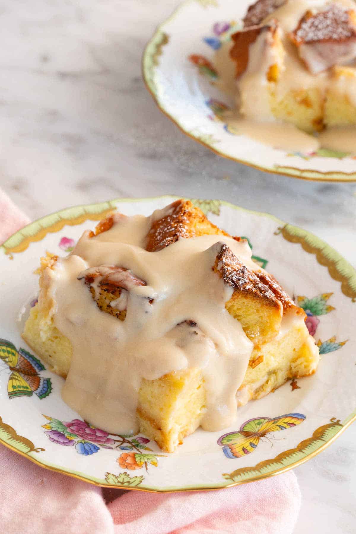 A plate with a serving of bread pudding with a second one in the background, slightly out of frame.