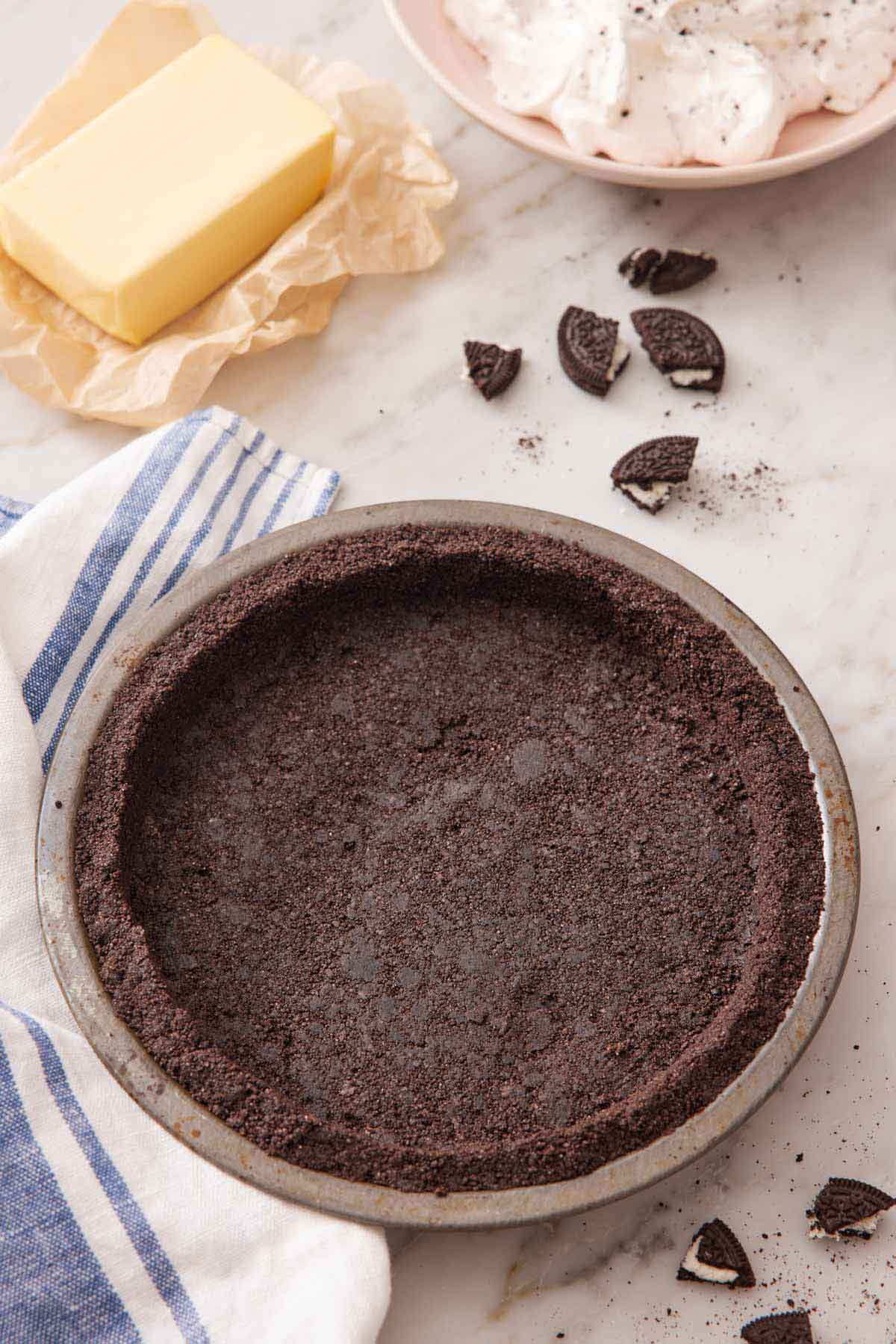 Overhead view of an Oreo pie crust in a pie pan and some Oreos, butter, and whipped topping in the background.