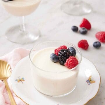 A plate with a glass of panna cotta topped with berries. More cups of panna cotta in the background.