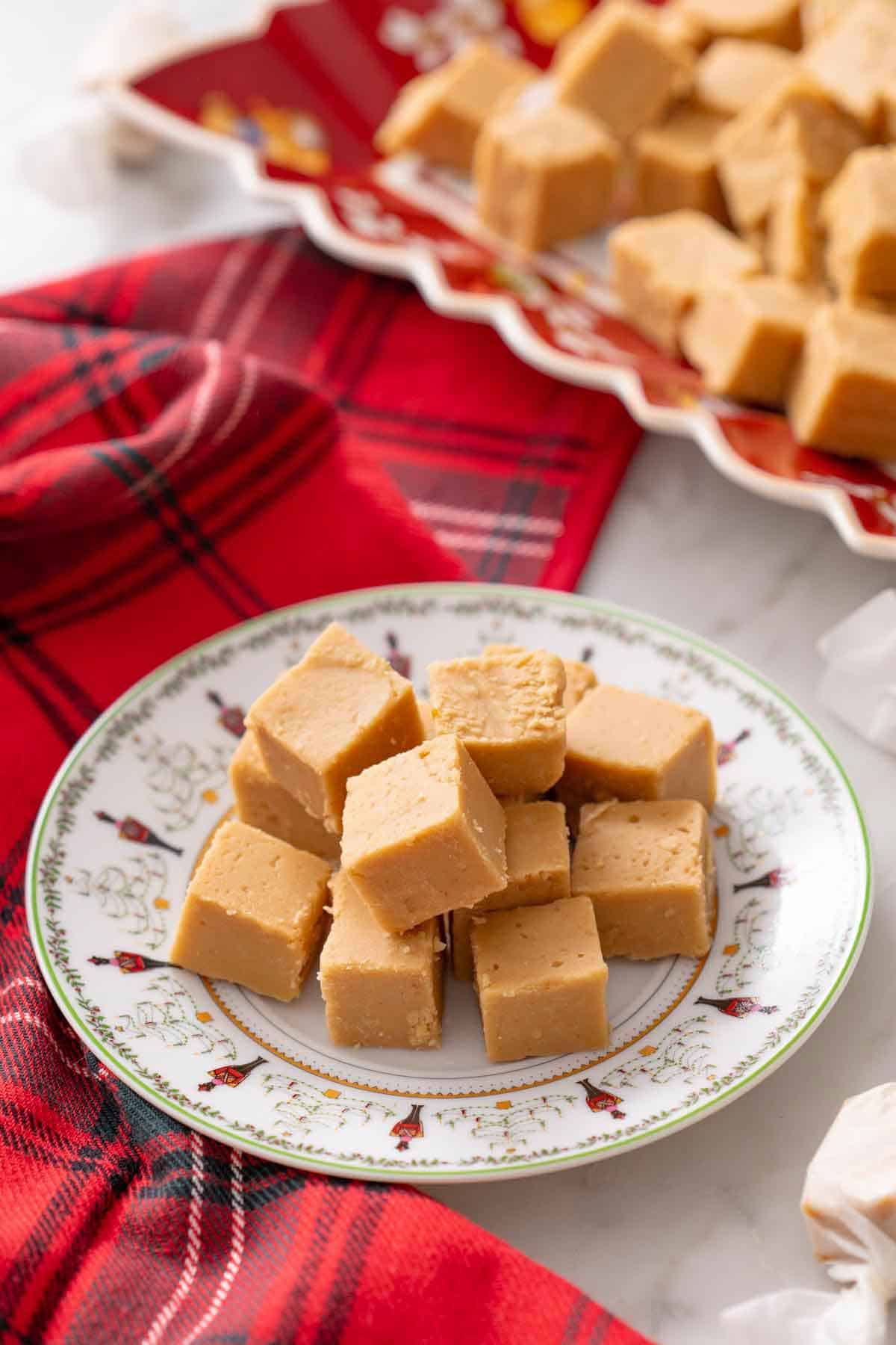 A plate with multiple pieces of peanut butter fudge with more on a platter in the background.
