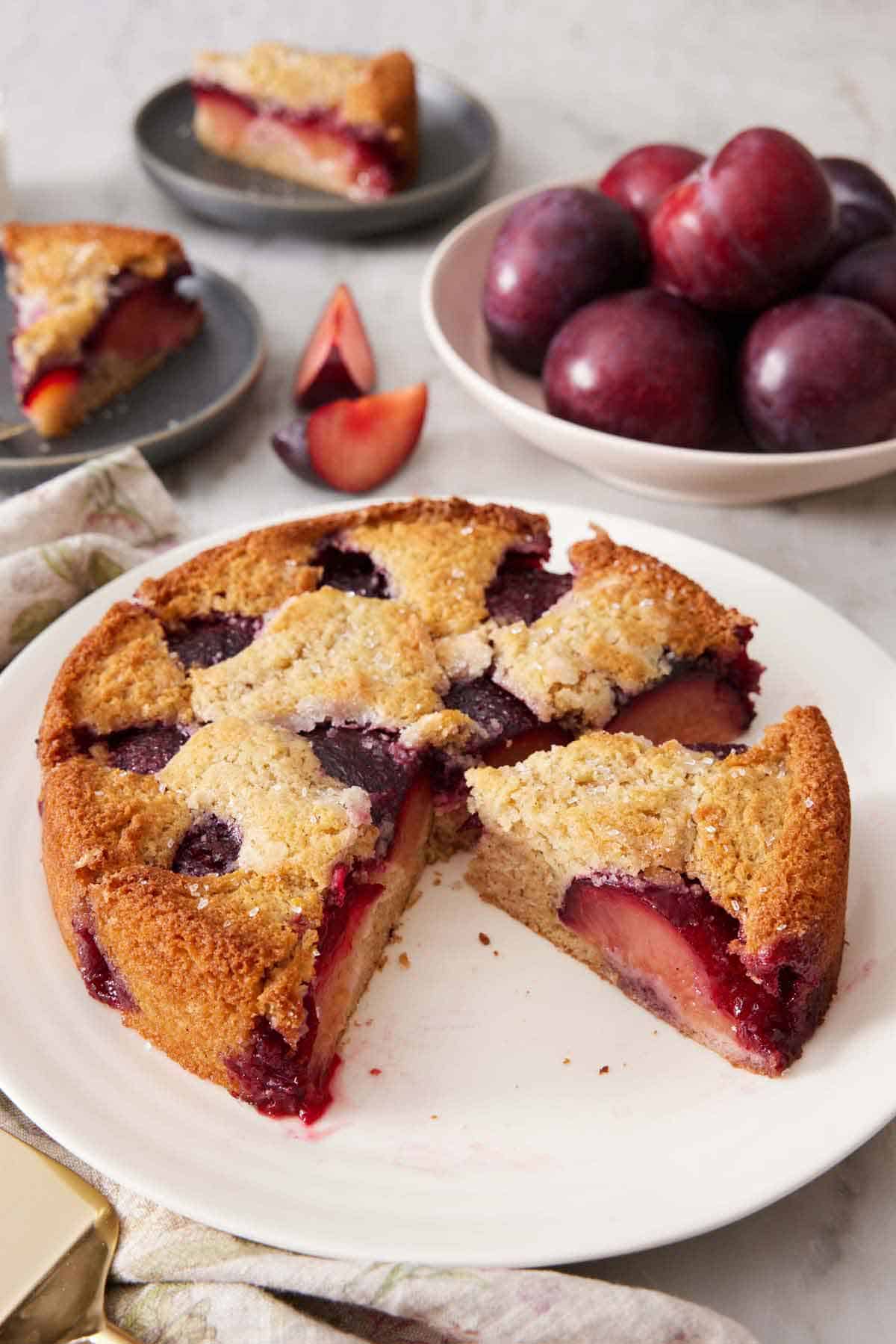 A platter with a cut plum cake with one slice cut and still on the platter.