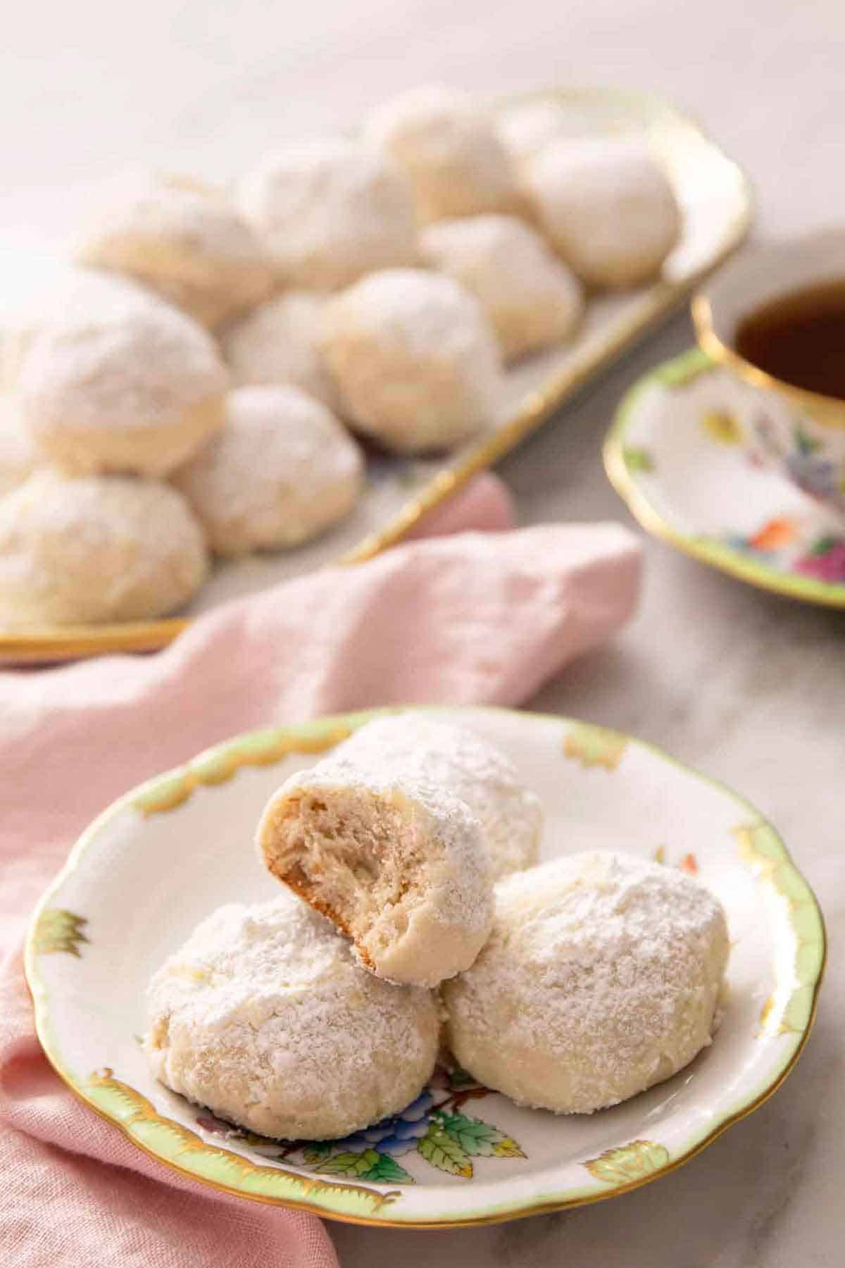 A plate with multiple Russian tea cakes with the one on top with a bite taken out of it. A platter more in the background.