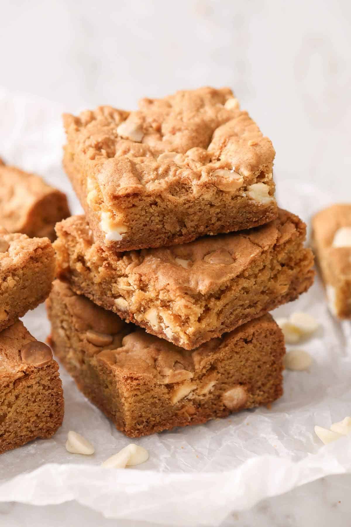 Three blondies stacked on parchmemt paper. More blondies off to the side.