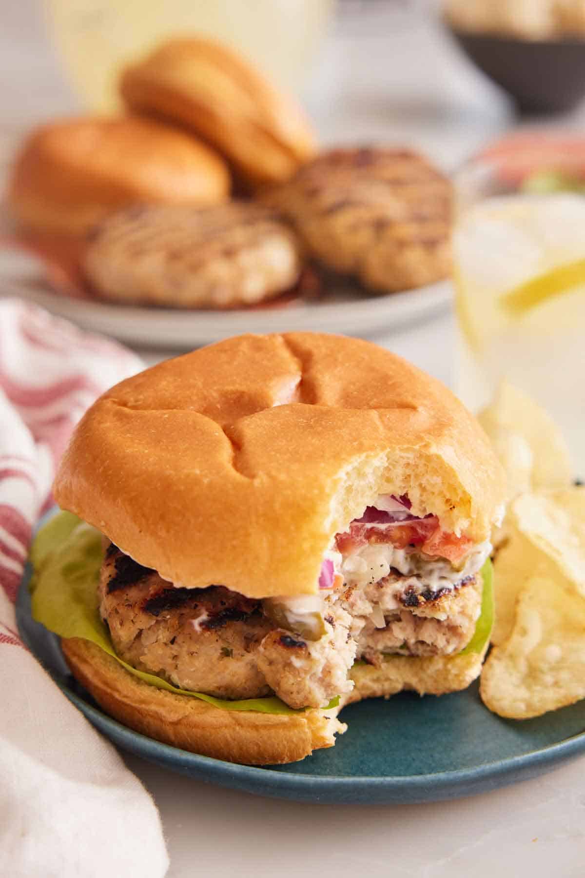 A plate with a chicken burger with a bite taken out.