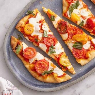 Overhead view of flatbread pizza on a platter cut into triangles. A linen napkin on the side.
