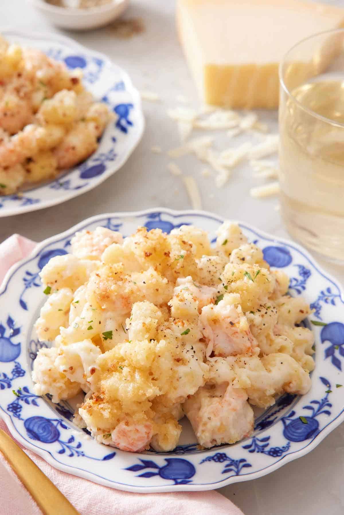 A plate of lobster mac and cheese with a glass in the background along with a block of parmesan.