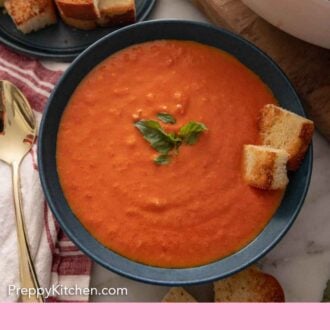 Pinterest graphic of an overhead view of a bowl of tomato soup with basil and bread on top.