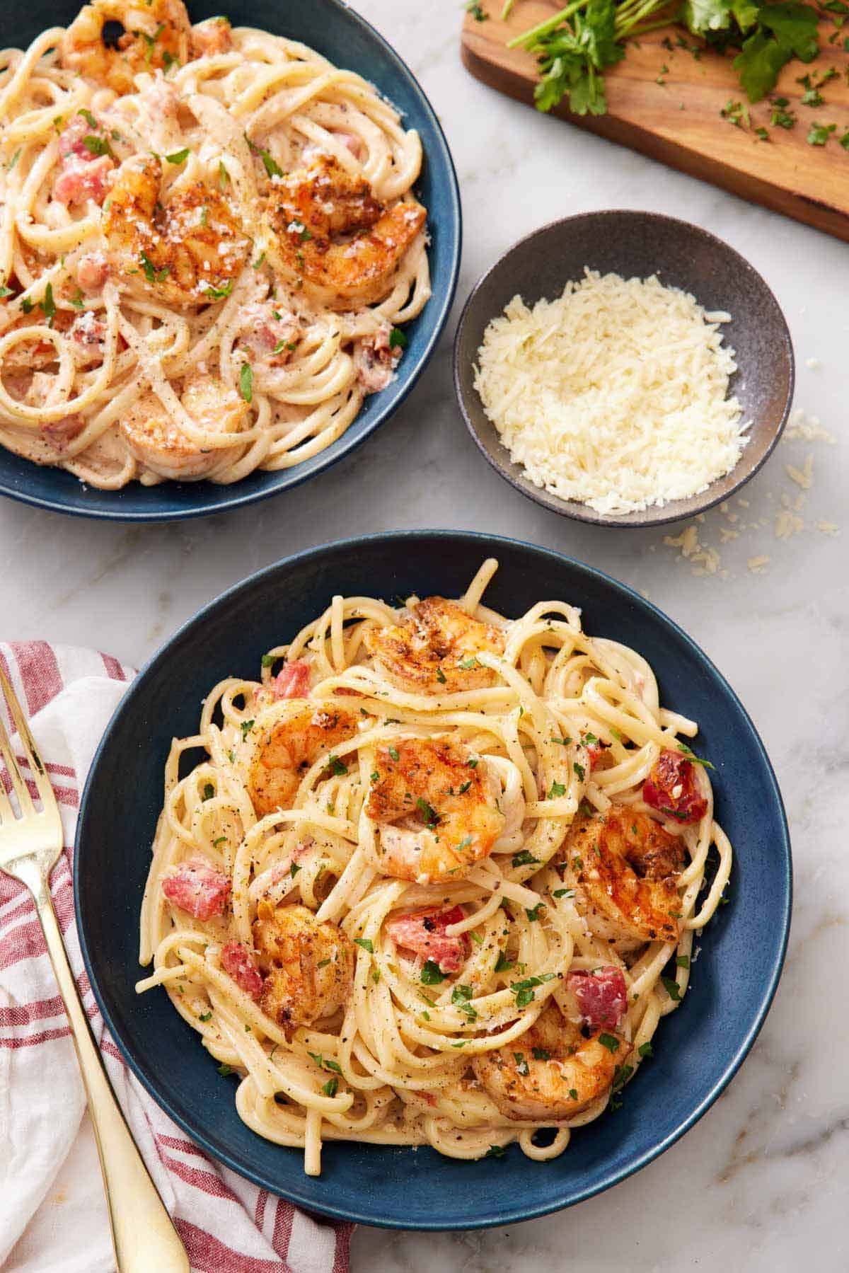 Two plates of cajun shrimp pasta with a bowl of shredded parmesan on the side.