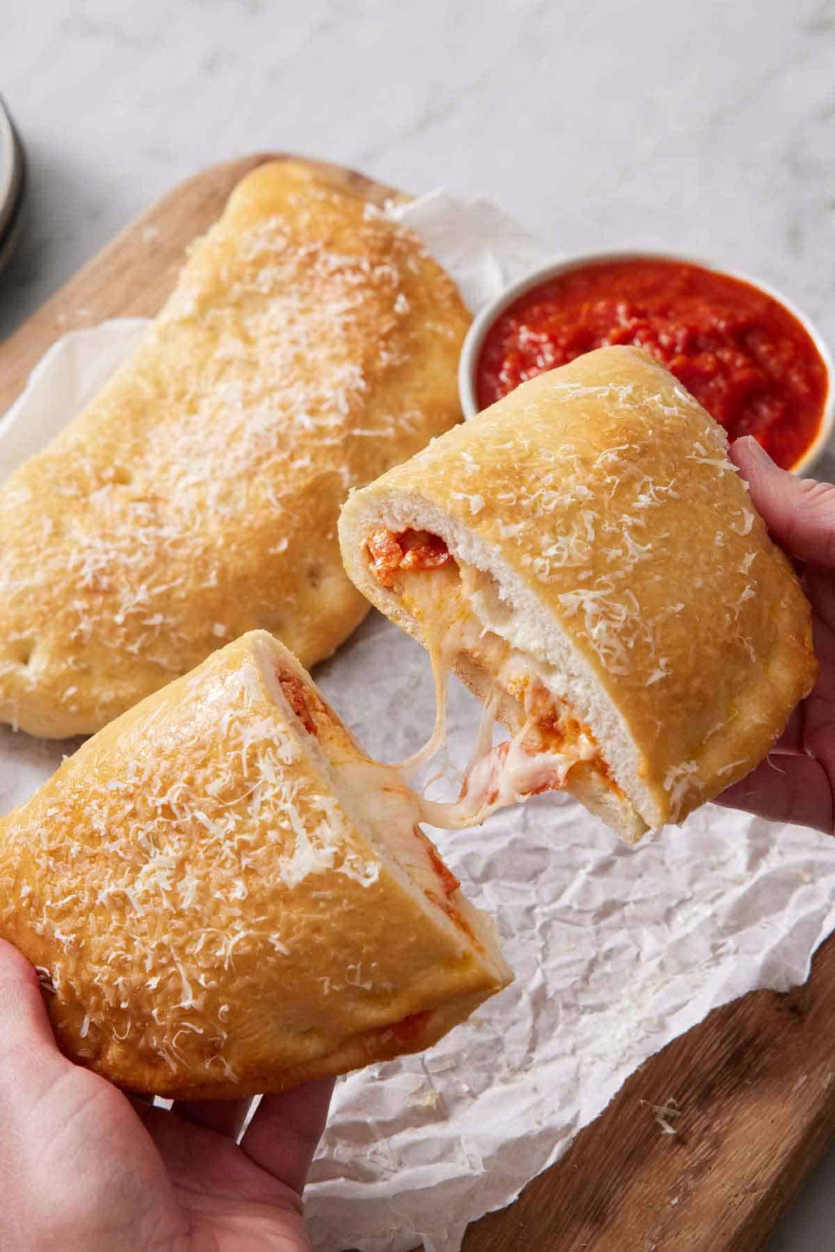 A half tearing apart of calzone with a melted cheese pull. Another calzone in the background.