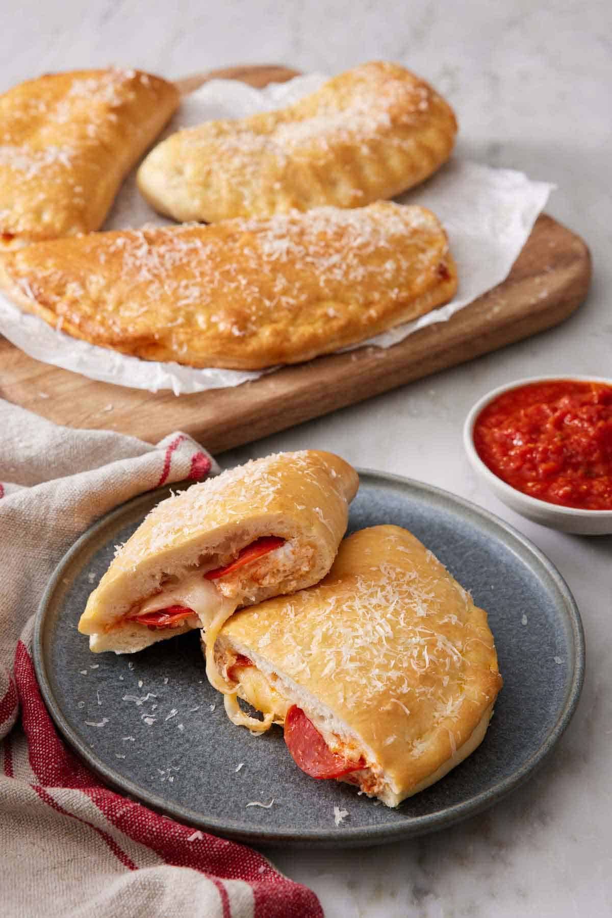 A plate with a calzone cut in half, showing the interior. More calzones in the background along with a bowl of sauce.