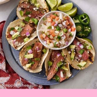 Pinterest graphic of an overhead view of a platter of steak tacos along with a bowl of salsa, lime wedges, and jalapenos.