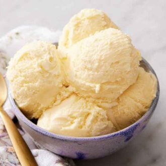 A bowl with scoops of vanilla ice cream with a spoon on the side.