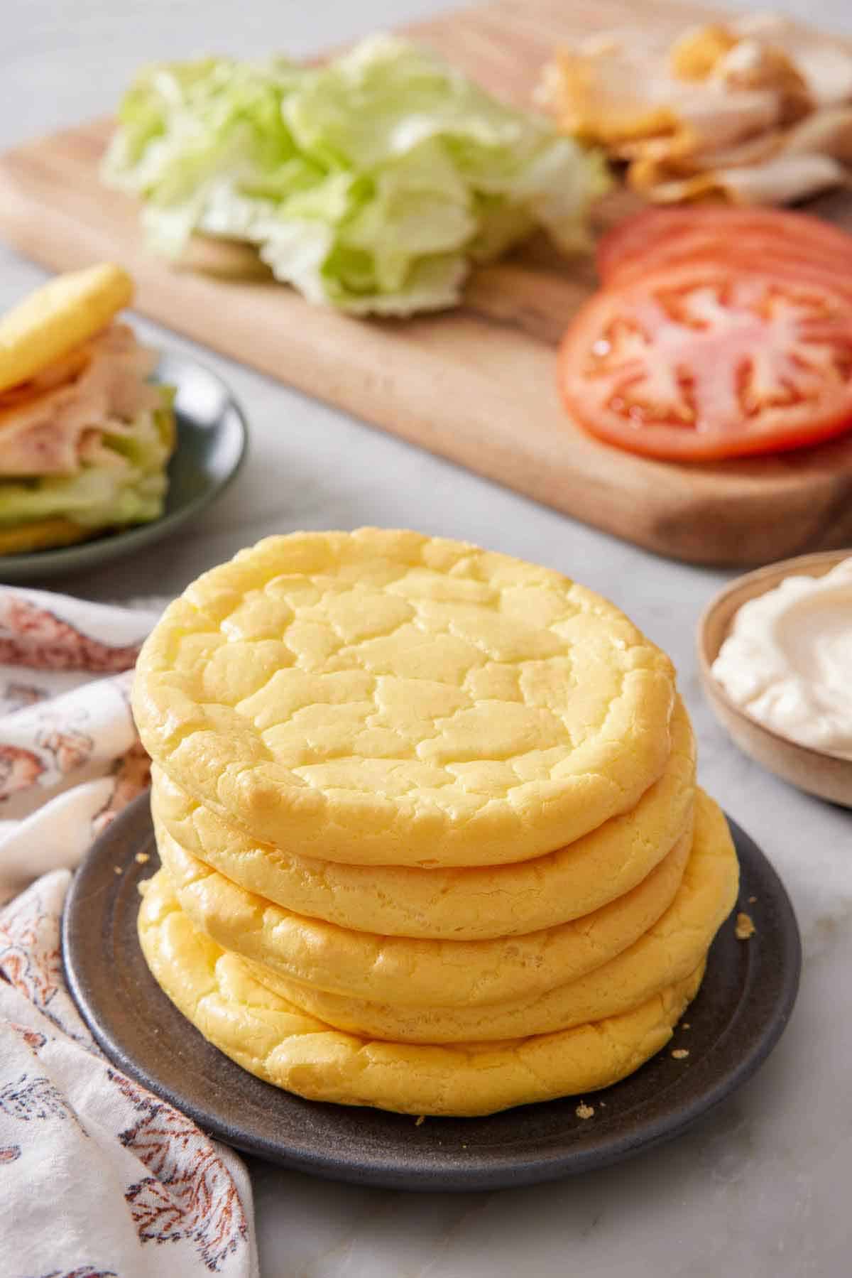 A plate with a stack of five cloud bread with sandwich fillings in the background.