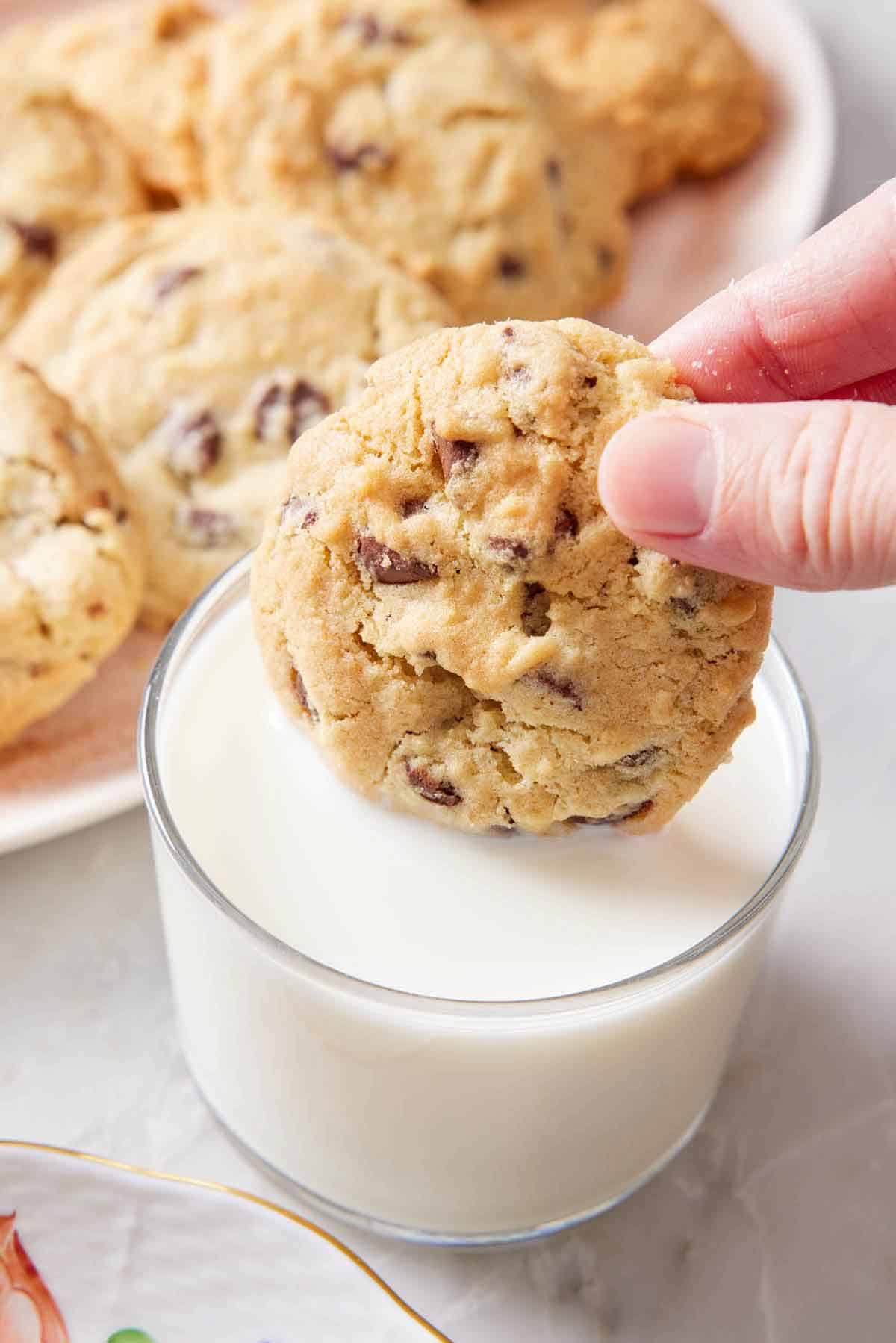 An air fryer cookie dunked into a glass of milk. More cookies in the background.