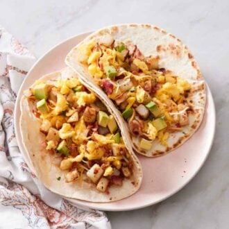 A plate with two breakfast tacos with a napkin beside it.