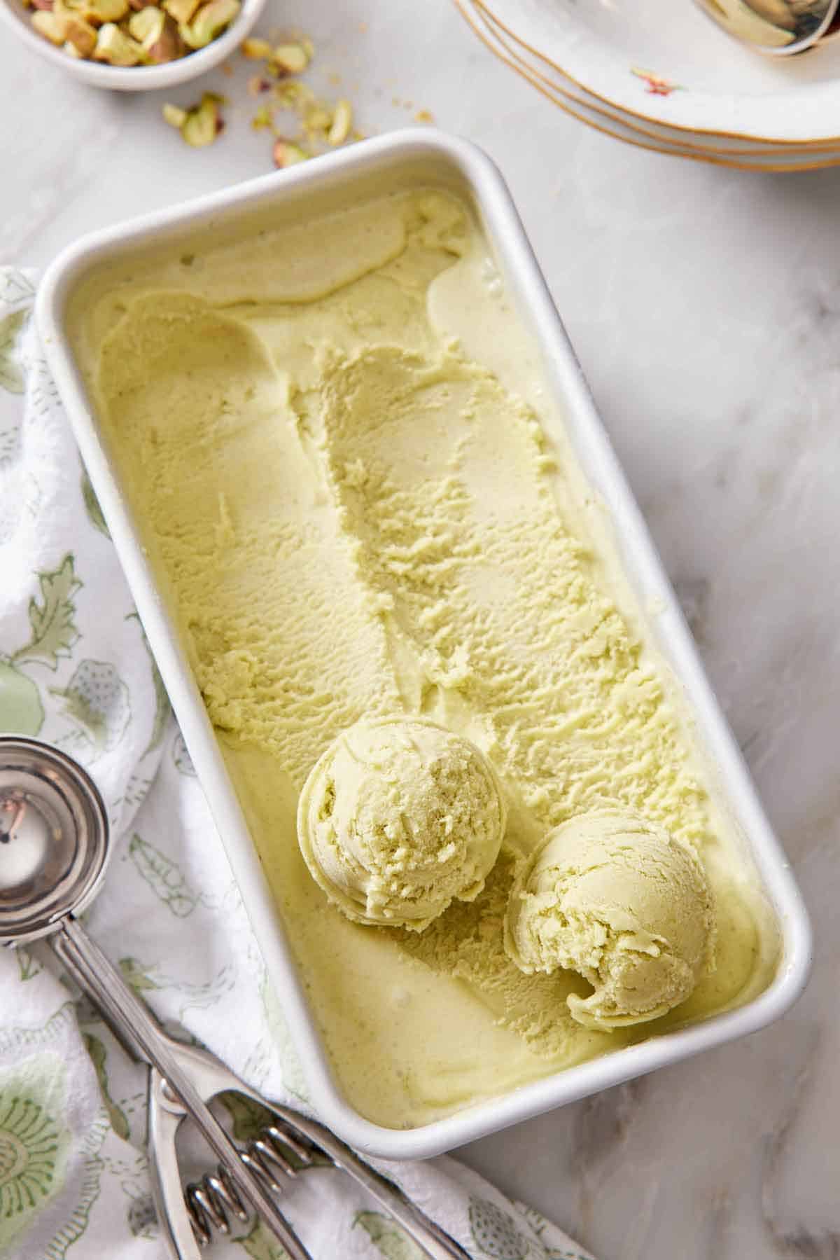 Overhead view of pistachio ice cream in a container with two balls of ice cream on top.