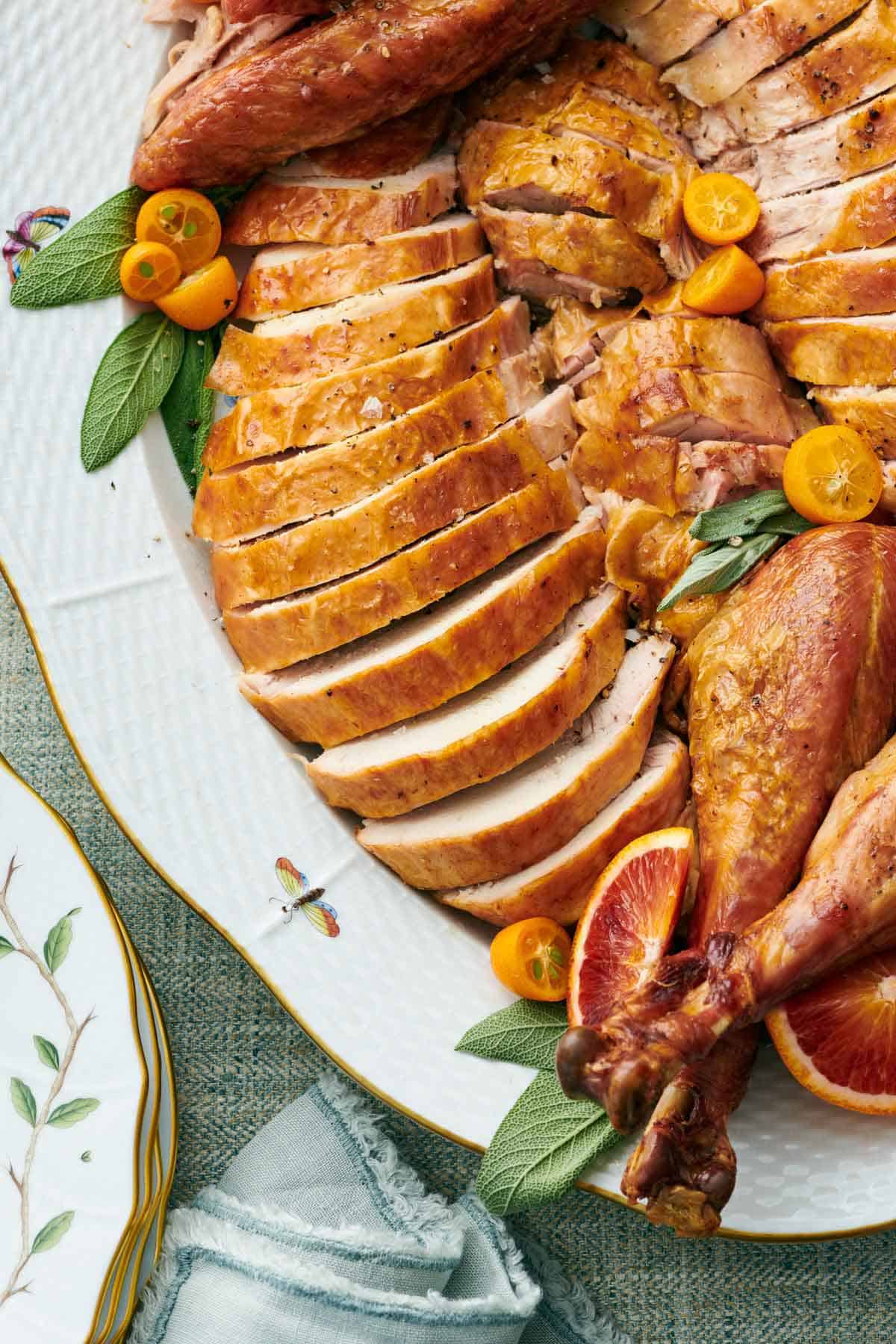 Overhead view of a platter of carved turkey with a focus on the turkey breasts. Sage and cut fruit on the platter.