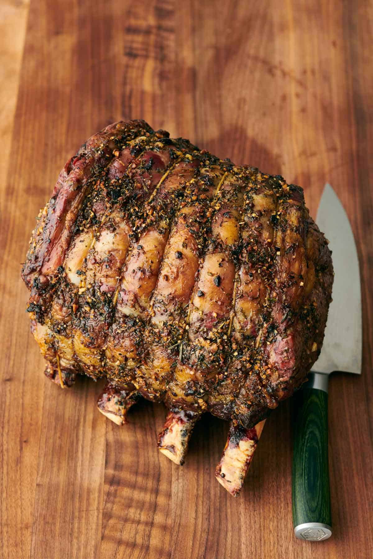 A prime rib on a wooden cutting board with a knife beside it.