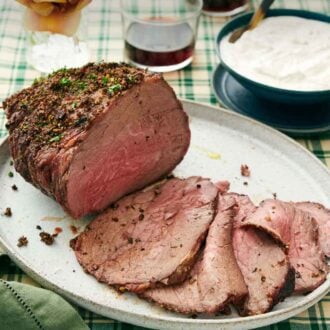 Pinterest graphic of a platter with a roast beef with half of it sliced in front. A bowl of sauce, drinks, and flowers in the back.