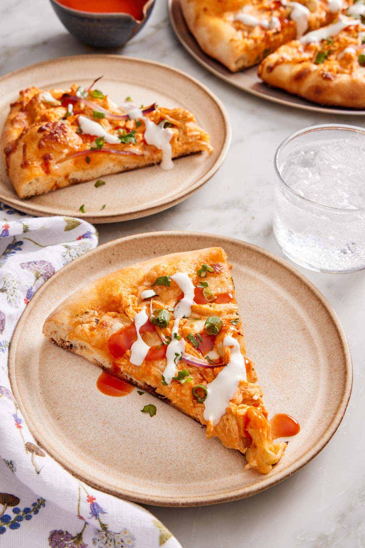 Two plates of buffalo chicken pizza with ranch and buffalo sauce drizzled on top. A soda in the background along with the rest of the pizza.