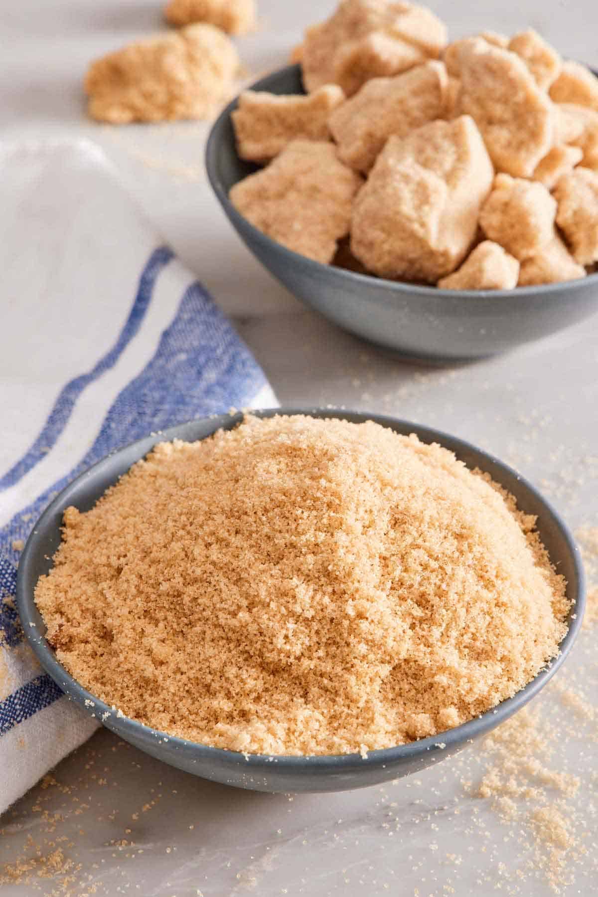 A bowl of softened brown sugar with a bowl of hardened brown sugar in the background.