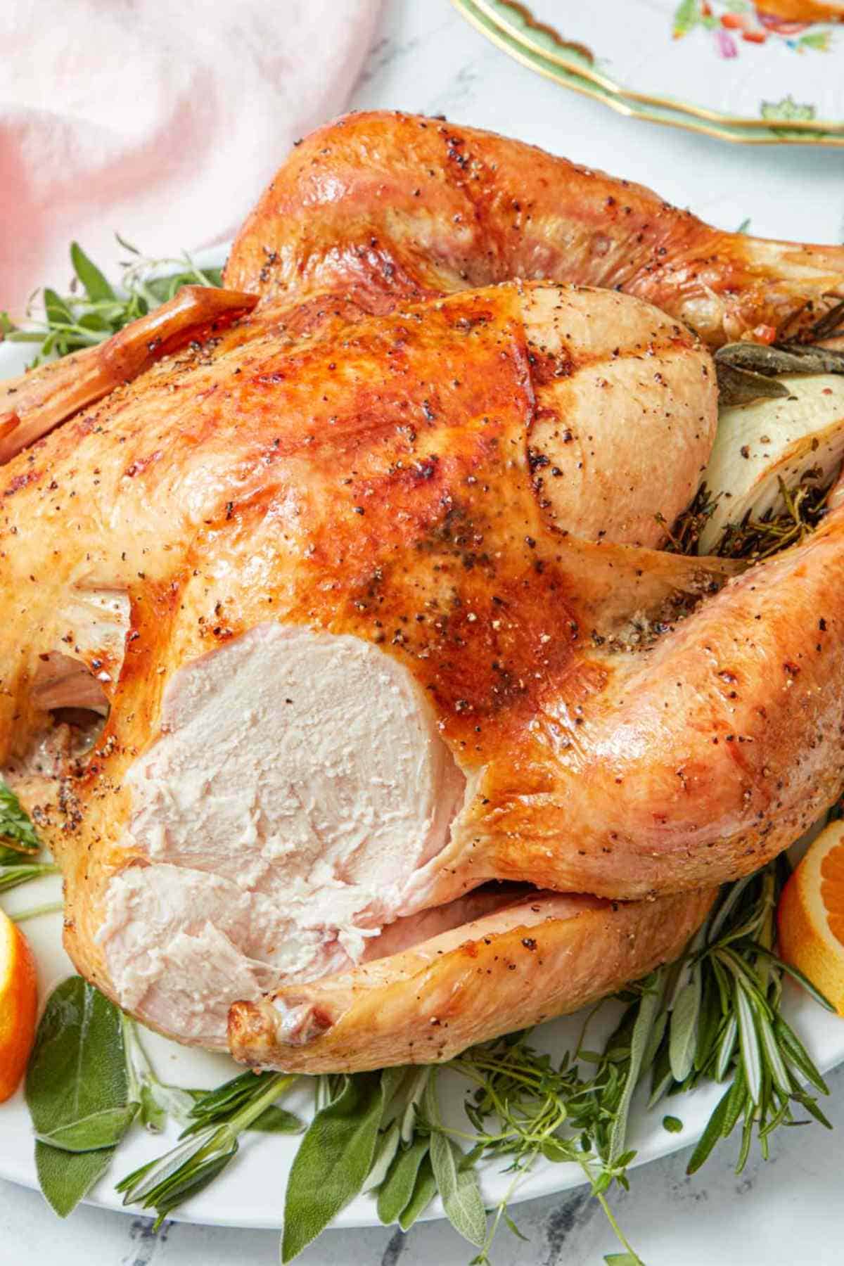 A roasted turkey on a bed of fresh herbs with a piece of the breast sliced off.